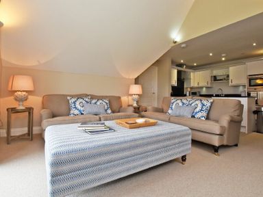 A living room with two sofas a large ottoman and a kitchen area at Sandpiper Bamburgh