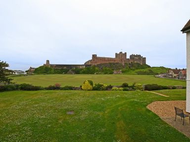 A large green lawn with a historic castle in the background and a partially visible house with a chair on the right side at Sandpiper Bamburgh