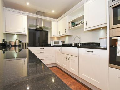 A kitchen with white cabinets black countertops a sink microwave kettle and built in oven at Sandpiper Bamburgh