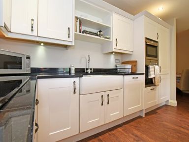 A kitchen with white cabinets a black countertop a microwave an oven a sink and wooden floor at Sandpiper Bamburgh