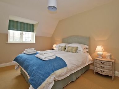 A bedroom with a made bed with blue throw and folded towels beside a window with a striped blind and a bedside table with a lamp at Sandpiper Bamburgh
