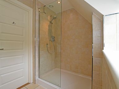 A tiled shower with a glass door and a wall-mounted showerhead at Sandpiper Bamburgh