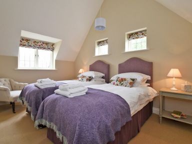 A bedroom with two single beds with purple blankets and floral pillows at Sandpiper Bamburgh