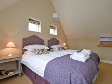 A bedroom with two single beds with purple headboards and blankets and bedside tables with lamps at Sandpiper Bamburgh