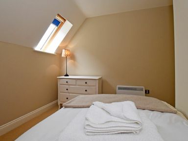 A bedroom with a bed of folded towels and blanket a white chest of drawers with a lamp and a slanted window at Sandpiper Bamburgh