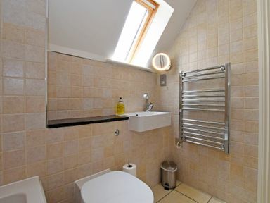 A bathroom with a wall-mounted sink a toilet a towel radiator and a skylight window at Sandpiper Bamburgh