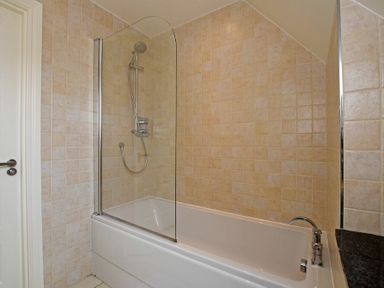 A bathroom with a bathtub shower combination and beige tiled walls at Sandpiper Bamburgh