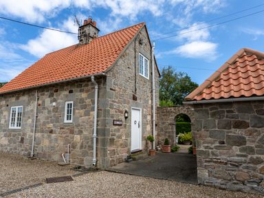 A stone house with a red tiled roof and a courtyard at Mid Cote in Shoreston near Bamburgh