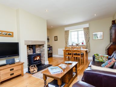 A living room with a wood stove fire television wooden furniture and a dining table at Mid Cote Shoreston near Bamburgh