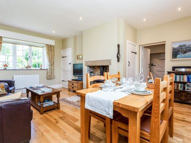 A dining area with a wooden table set with dishes and glasses next to a living room with chairs coffee table and a fireplace at Mid Cote in Shoreston near Bamburgh