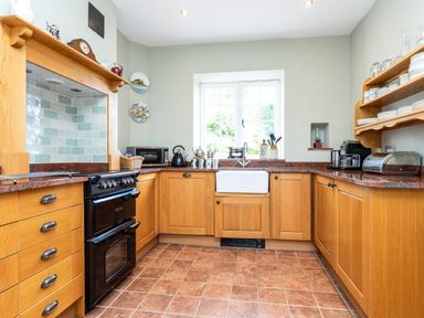 A kitchen with wooden cabinets a black oven a white sink and a window above it at Mid Cote Shoreston near Bamburgh