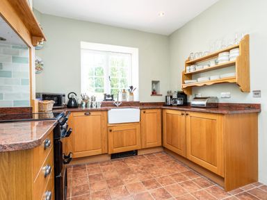 A kitchen with wooden cabinets a tiled floor a window above a sink and kitchen appliances at Mid Cote in Shoreston near Bamburgh