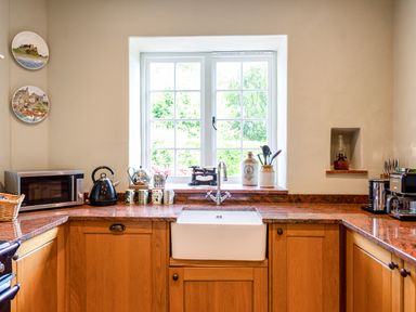 A kitchen with wooden cabinets a white sink and a window above at Mid Cote Shoreston near Bamburgh