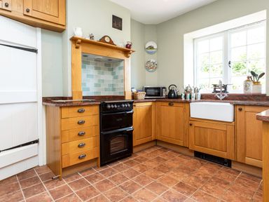 A kitchen with wooden cabinets a black oven a white sink and a window at Mid Cote Shoreston near Bamburgh