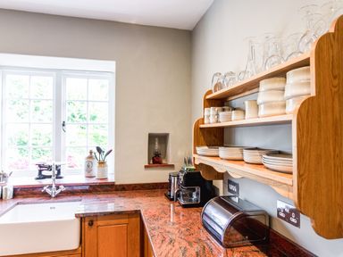 A kitchen counter with sink toaster coffee machine open wooden shelves with dishes glasses and bowls at Mid Cote Shoreston near Bamburgh