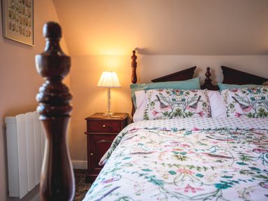 A bedroom with a bed with floral bedding and a wooden nightstand with a lamp at Mid Cote Shoreston near Bamburgh