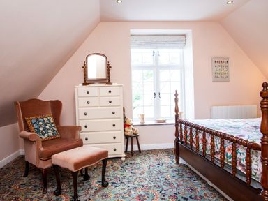 A bedroom with a wooden bed a white chest of drawers an upholstered armchair with matching footstool and a window at Mid Cote in Shoreston near Bamburgh