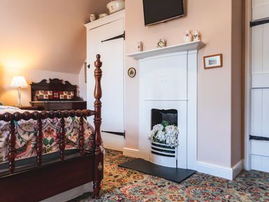 A bedroom with a wooden bed a floral bedspread a white fireplace with flowers inside and a lamp on a side table at Mid Cote in Shoreston near Bamburgh