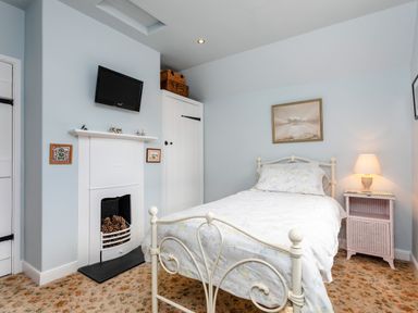 A bedroom with a single bed a nightstand with a lamp a wall-mounted TV and a decorative fireplace at Mid Cote Shoreston near Bamburgh