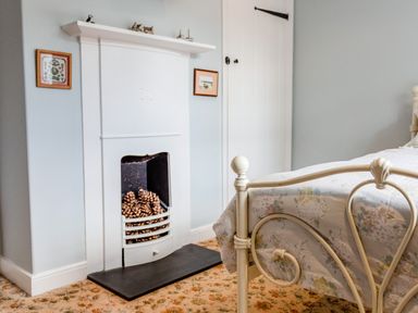 A bedroom with a metal bed frame a fireplace with pine cones and a cupboard at Mid Cote in Shoreston near Bamburgh