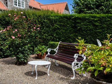 A garden with a wooden bench with white metal armrests and a white metal table on a gravel ground at Mid Cote Shoreston near Bamburgh