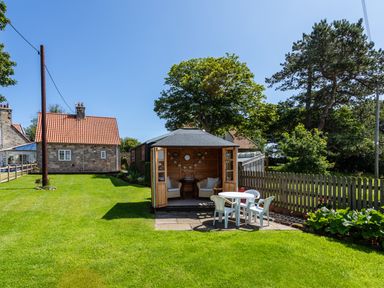 A garden with a wooden summerhouse and white plastic table and chairs at Mid Cote Shoreston near Bamburgh