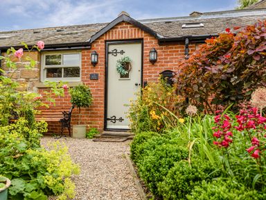 A brick cottage front door with decorative plants and flowers along a gravel path at Nurses Cottage in Alnwick