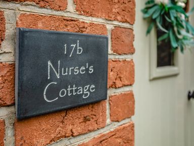 A black plaque with 17b Nurse's Cottage on a red brick wall next to a door with a wreath at Nurse's Cottage in Alnwick