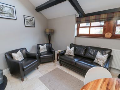 A seating area with two armchairs and a sofa with cushions a floor lamp and framed pictures on the wall at Nurses Cottage in Alnwick