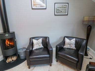 Two black leather armchairs with patterned cushions between a wood stove and a tall floor lamp in a sitting room at Nurses Cottage in Alnwick