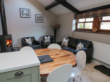 A sitting area with black leather chairs and sofa around a wooden round table near a wood burning stove at Nurses Cottage in Alnwick