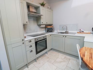 A kitchen with green cabinets a built-in oven a microwave a sink and a wooden table at Nurses Cottage in Alnwick