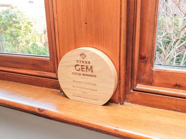 A wooden award on a wooden window sill with a garden visible through the window at Nurse's Cottage in Alnwick