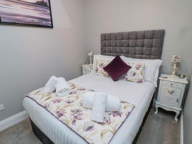 A bedroom with a double bed white bedside tables and folded towels at Nurse's Cottage in Alnwick