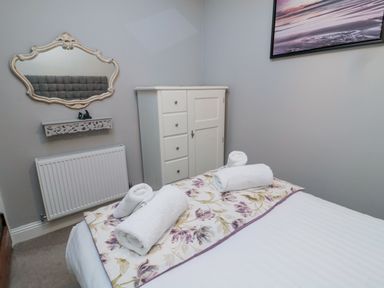 A bedroom with a bed with rolled towels on floral runner a white chest of drawers and a wall mirror at Nurse's Cottage in Alnwick