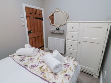 A bedroom with a wooden door a white wardrobe a wall mirror and a bed with rolled white towels on a floral runner at Nurses Cottage in Alnwick