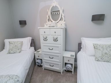 A bedroom with two single beds white bedding floral pillows white chest of drawers and bedside tables at Nurse's Cottage in Alnwick
