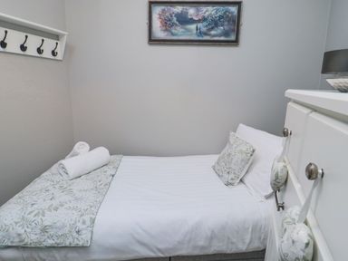A small bedroom with a single bed white bedding floral pillow and blanket painting on wall at Nurses Cottage in Alnwick