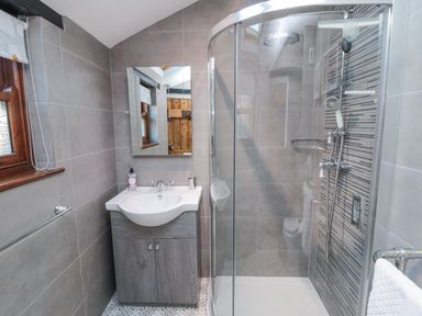 A bathroom with a sink vanity unit mirror glass shower enclosure and a towel rail at Nurses Cottage in Alnwick