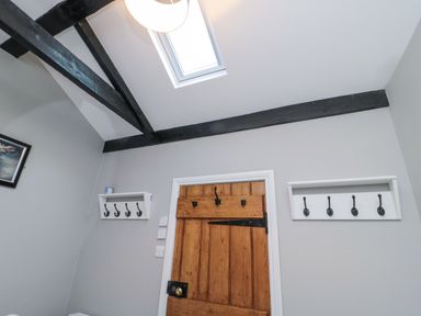 A room with a wooden door white walls black ceiling beams two white racks with hooks and a skylight at Nurse's Cottage in Alnwick