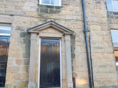 A black wooden door with stone columns and triangular stone pediment on a stone building at Nurse's Cottage in Alnwick