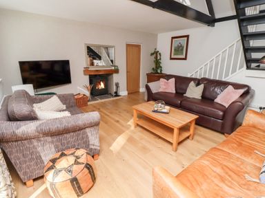 A living room with sofas a coffee table a wall-mounted television a fireplace and stairs at Old Stable Cottage in Alnmouth
