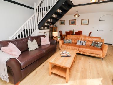 A living room with two sofas and a wooden coffee table under a staircase at Old Stable Cottage in Alnmouth