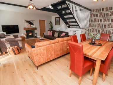A living and dining area with sofas a fireplace a television a wooden dining table and red chairs at Old Stable Cottage in Alnmouth