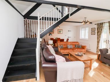 A living room with black stairs white railings two sofas a wooden coffee table and a dining area at Old Stable Cottage in Alnmouth