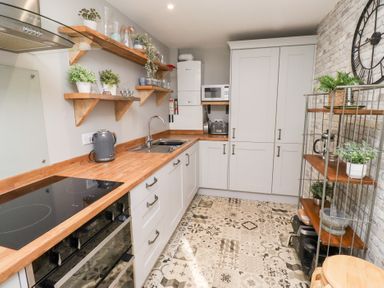 A kitchen with wooden countertops white cabinets patterned floor and shelves with plants at Old Stable Cottage in Alnmouth