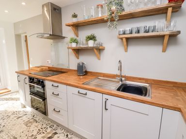 A kitchen with wooden countertops shelves with cups and plants and a sink at Old Stable Cottage in Alnmouth