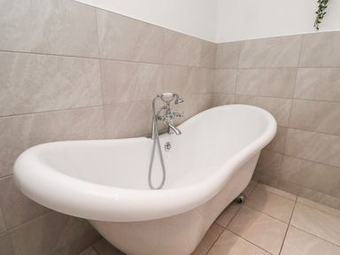 A white freestanding bathtub with a silver faucet and shower hose in a tiled bathroom at Old Stable Cottage in Alnmouth