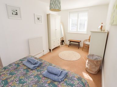 A bedroom with a bed with folded towels a white wardrobe a rattan chair and a chest of drawers at Old Stable Cottage in Alnmouth