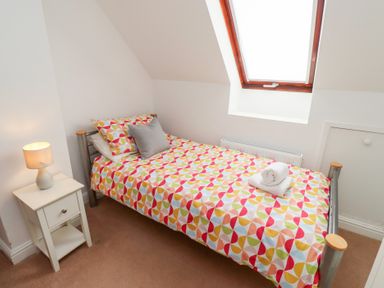 A bedroom with a single bed beside a window and a nightstand with a lamp at Old Stable Cottage in Alnmouth